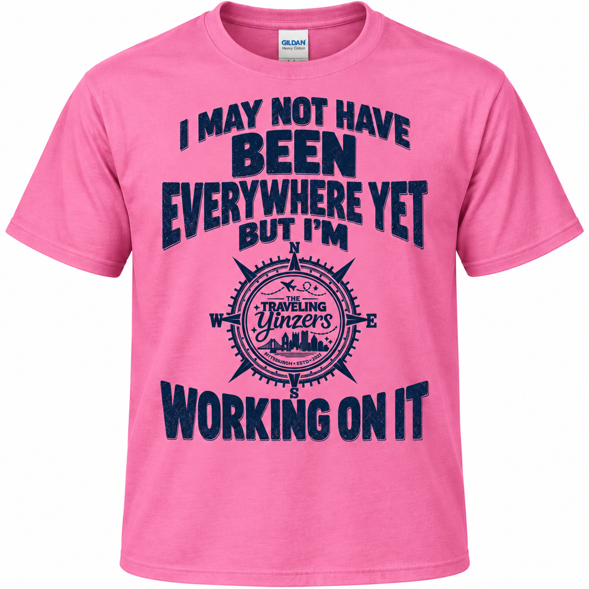 A pink short-sleeve t-shirt with a dark navy blue graphic print on the front. The graphic features a compass design with the text 'I MAY NOT HAVE BEEN EVERYWHERE YET BUT I'M WORKING ON IT' and a circular emblem reading 'TRAVELING Yinzer's Way'.